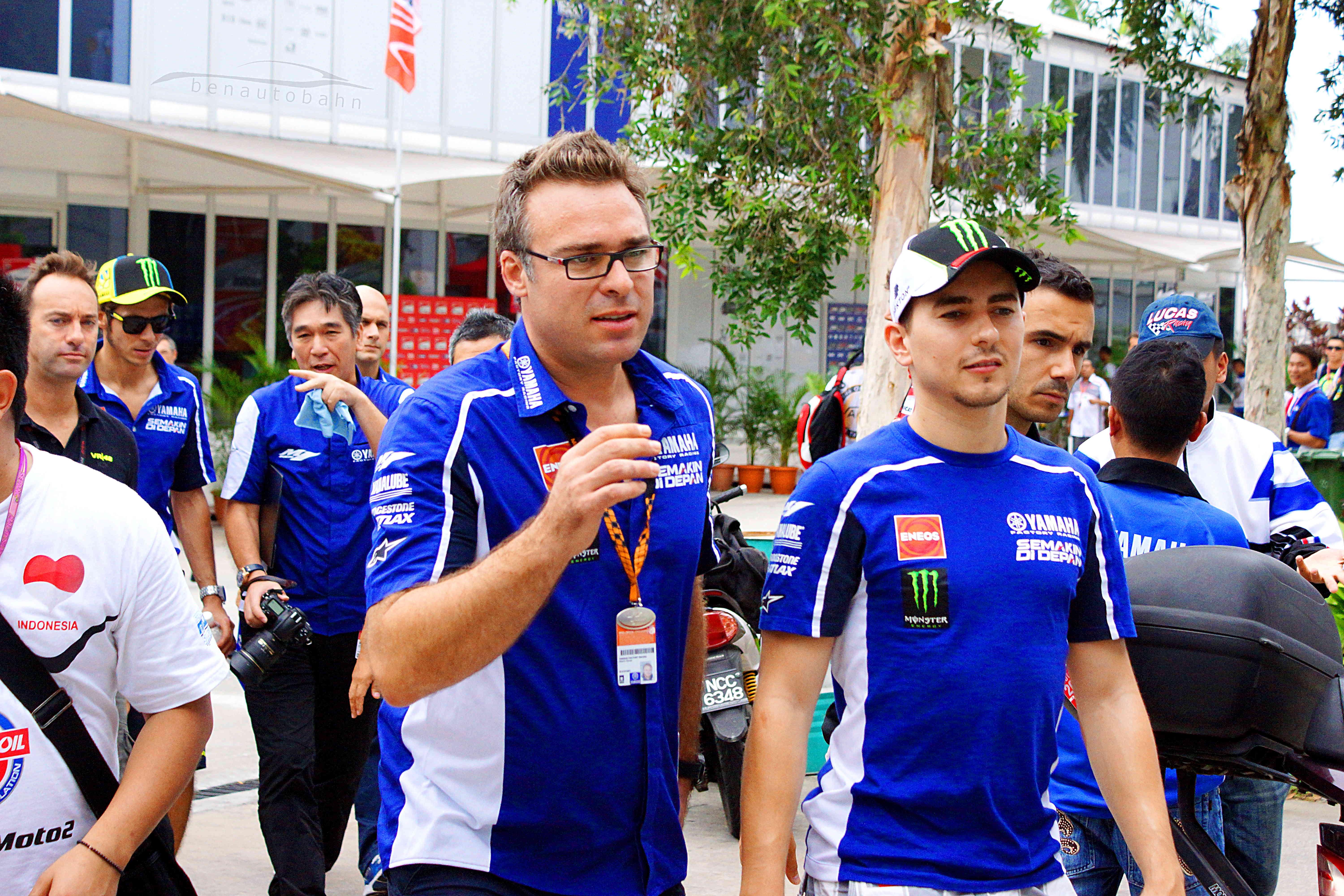 Jorge Lorenzo (right), and Valentino Rossi (rear left, both wearing caps) chatting with their team.